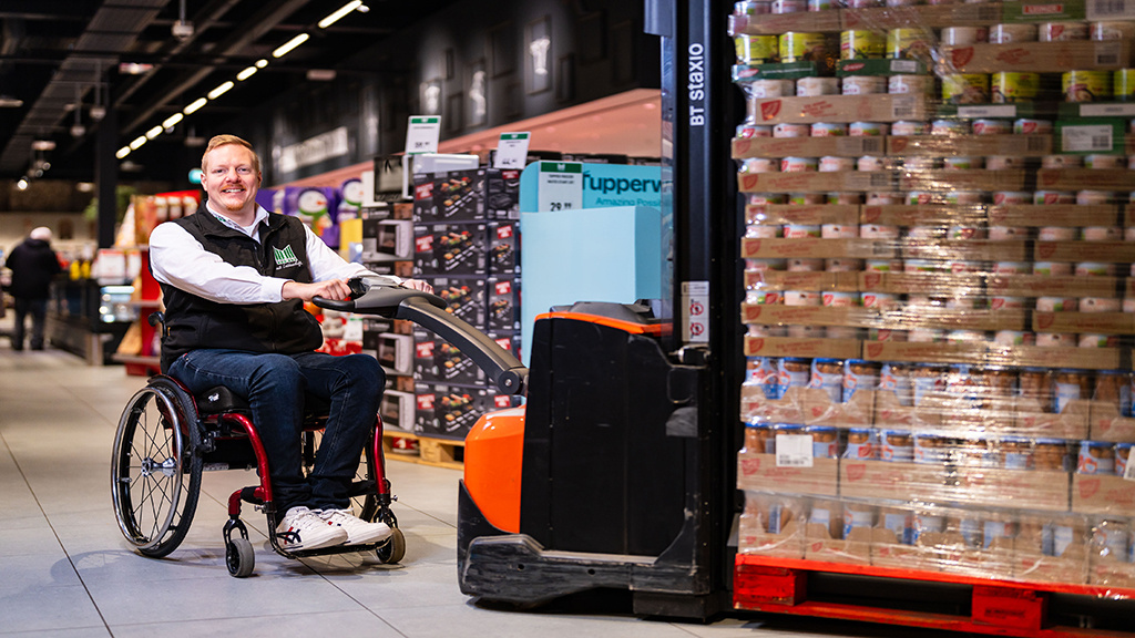 Ein Mann im Rollstuhl fährt einen Gabelstapler.